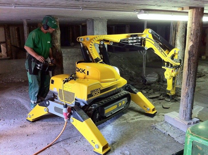 En operat%C3%B8r styrer en gul Brokk 100 rivningsrobot under et rivearbeid innend%C3%B8rs.
